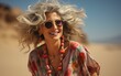 © imagineRbc - A woman with a flowery dress and a necklace with red beads is smiling. She is wearing sunglasses and has her hair blowing in the wind. The scene is set in a desert