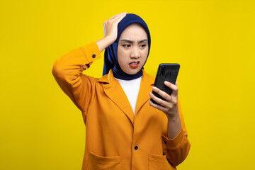 Wall Mural - Upset young Asian woman looking at mobile phone screen with worried expression, reading negative message isolated on yellow background