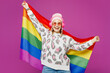 © ViDi Studio - Young happy lesbian woman wear pink animal clothes listen to music in headphones hold rainbow striped flag isolated on plain purple background studio portrait. Pride day June month love LGBTQ concept.