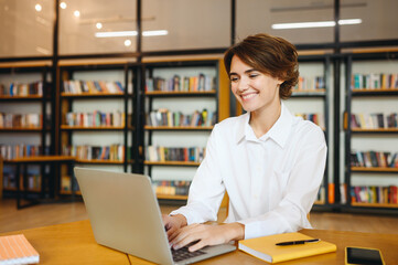 Canvas Print - Young smiling cheerful happy successful employee IT business woman wear white shirt casual clothes hold use work on laptop pc computer surfing internet sit at office desk. Achievement career concept.