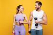© ViDi Studio - Young strong fitness trainer instructor two man woman wear blue clothes spend time in home gym hold in hand dumbbells look to each other isolated on plain yellow background. Workout sport fit concept.