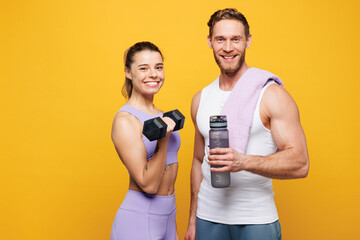 Wall Mural - Young strong fitness trainer instructor sporty two man woman wearing blue clothes spend time in home gym hold in hand dumbbell bottle of water isolated on plain yellow background Workout sport concept