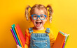 © Viktoriia - Cheerful young girl with blue glasses holding colorful school supplies against a bright yellow background, ready for school and learning