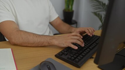 Poster - Young hispanic man working on a computer at an office desk with plants in the background.