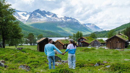 Wall Mural - A couple walks hand in hand in front of traditional Norwegian cabins with a stunning mountain backdrop. Innerdalen Norway most beautiful mountain valley