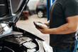 © CanBorg/peopleimages.com - Electrical, test and mechanic in workshop with car, maintenance or checking motor in service shop. Volt meter, engine and man in garage with machine for inspection, auto repair and quality assurance