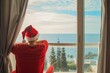 © alisaaa - Man in hotel room celebrating chritmas, he opens the curtains in the morning looking at the sea view, he is wearing a santa hat Man in hotel room celebrating chritmas, he opens the curtains in the mor
