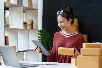 Happy asian woman runs a small online business from her office, managing shipping, inventory, and customer service with a tablet