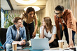 © LIGHTFIELD STUDIOS - A diverse group of colleagues from a startup team engaging in discussion and teamwork around a laptop in a modern business setting.