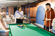 © LIGHTFIELD STUDIOS - A group of colleagues from a startup team enjoying a game of pool in a modern business setting.