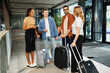 © LIGHTFIELD STUDIOS - Multicultural colleagues in casual attire standing around with luggage in a hotel lobby during a corporate trip.