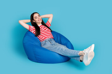 Wall Mural - Full length photo of adorable lovely girl wear striped t-shirt relaxing bean bag arms behind head empty space isolated blue color background