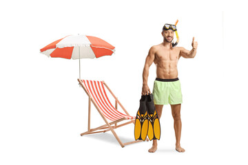 Sticker - Beach chair and umbrella and young man in swimwear with a diving mask holding snorkeling fins and gesturing thumbs up