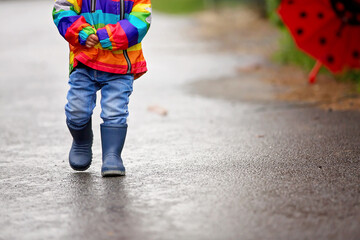 Sticker - Beautiful boy with rainbow raincoat, enjoying the rain in spring, holding umbrella