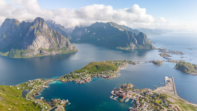 An aerial view of Reine, a picturesque village in the Lofoten Islands of Norway, showcasing the dramatic mountains, clear waters, and charming harbor. Reinebringen, Lofoten, Norway