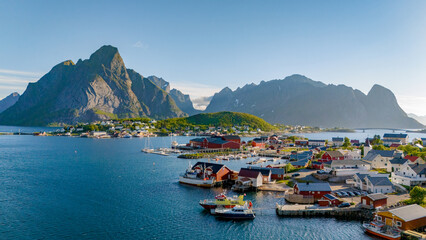 Wall Mural - A picturesque coastal village in Norway, surrounded by towering mountains, showcasing red-roofed houses and boats in the calm waters of a fjord. Reine, Lofoten, Norway