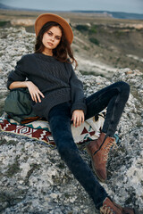 Wall Mural - Serene woman in hat and sweater perched on mountain rock, contemplating the breathtaking view