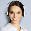 © vgstudio - Call center help line service. Portrait of customer support phone sales operator in headset, isolated against grey gray wall background. Happy smiling business woman. Caller worker. Square image.