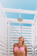 © svetograph - A woman in a bikini stands in front of a white shower stall. She is smiling and she is enjoying the moment.