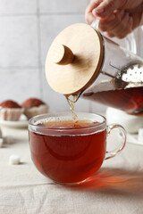 Wall Mural - Woman pouring tea into cup at light table, closeup