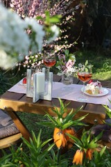 Canvas Print - Vase with spring flowers, wine and cake on table served for romantic date in garden