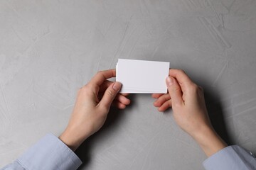 Sticker - Woman holding blank cards at light grey table, top view. Mockup for design