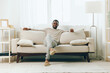 © SHOTPRIME STUDIO - Relaxed African American Man Sitting on Sofa at Home, Lost in Thought, Exuding a Sense of Sadness but Finding Comfort in the Coziness of His Living Room The Modern Interior Provides a Peaceful
