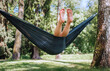 © Soloviova Liudmyla - Barefoott legs of Little girl enjoying sunny day swinging in hammock, surrounded by lush trees and green grass. Her joyful expression captures the essence of carefree childhood and outdoor