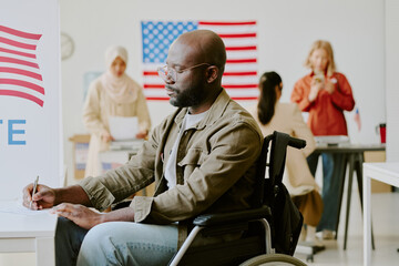 Medium shot of African American man with disability filling in ballot paper at polling station