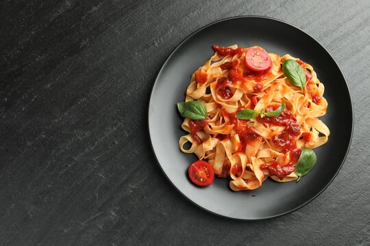 Delicious pasta with tomato sauce, vegetable and basil on dark textured table, top view. Space for text