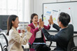 © amnaj - Business team celebrating success with high five in modern office. Diverse colleagues sharing a moment of achievement and joy.