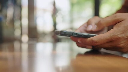 A person is holding a cell phone and looking at it. The phone is on a wooden table