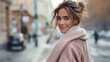 © Pinklife - A fashionable woman wearing a beige coat and a cozy scarf smiles while standing on a busy downtown street with a slight blur of urban activity in the background.