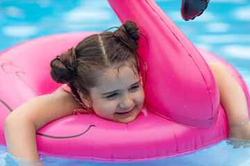 Wall Mural - Happy little child girl swimming with flamingo pink inflatable ring in clean pool water while having fun during vacation. Summer concept. Top view with copy space