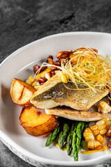 Wall Mural - Seared fish atop roasted potatoes, garnished with herbs, served in a white bowl on a textured grey surface