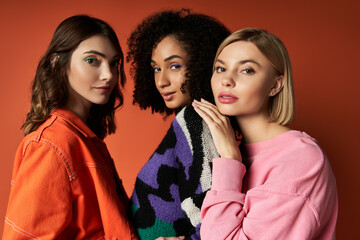 Wall Mural - Three young, multicultural women stand stylishly before a vibrant red backdrop, showcasing diversity in fashion and culture.