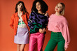 © LIGHTFIELD STUDIOS - A group of young, beautiful, multicultural women in stylish vibrant clothes pose together on an orange background, showcasing female friendship and cultural diversity.