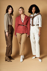 Wall Mural - Three young, beautiful women in stylish attire stand together, showcasing diversity and friendship on a beige background.