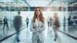 © Pinklife - A female professional stands with arms crossed, poised, amid a bustling, modern office environment with blurred figures of coworkers passing by, symbolizing leadership and confidence.