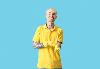 Poster - Young tattooed man putting rubber gloves on blue background