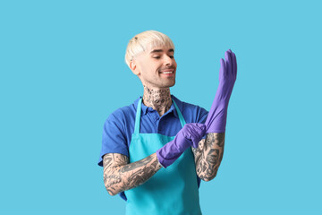 Poster - Young tattooed man putting rubber gloves on blue background