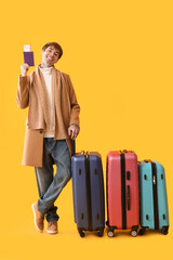 Wall Mural - Happy young man with passport, ticket and suitcases on yellow background