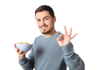 Poster - Handsome young man holding bowl with cereal rings and showing OK gesture on white background