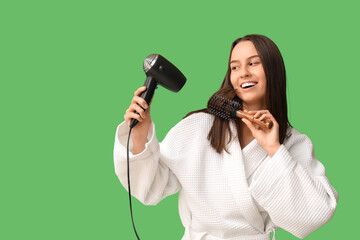 Poster - Beautiful young woman in bathrobe with hair dryer and brush on green background