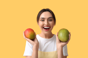 Wall Mural - Beautiful young woman with sweet mango fruits on yellow background