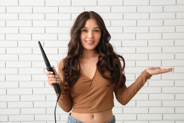 Sticker - Young Asian woman with curling iron showing something on white brick background