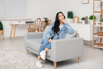 Canvas Print - Beautiful young woman with dark wavy hair sitting on sofa in living room