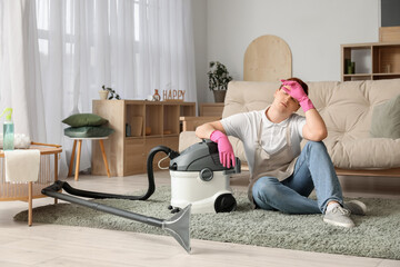 Wall Mural - Tired young man with vacuum cleaner sitting on floor in living room