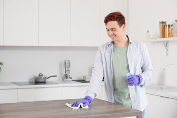 Wall Mural - Young man with rag and spray bottle cleaning table in kitchen