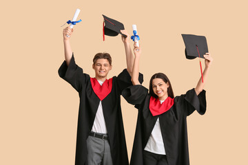 Wall Mural - Happy graduate couple with diplomas on beige background